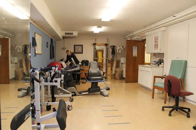 Photo of exercise equipment and a skilled nurse inside the physical therapy room at Pleasant View